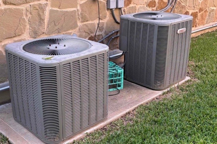Two new condensers set on a shared pad after a double system changeout at a Central Texas stone home