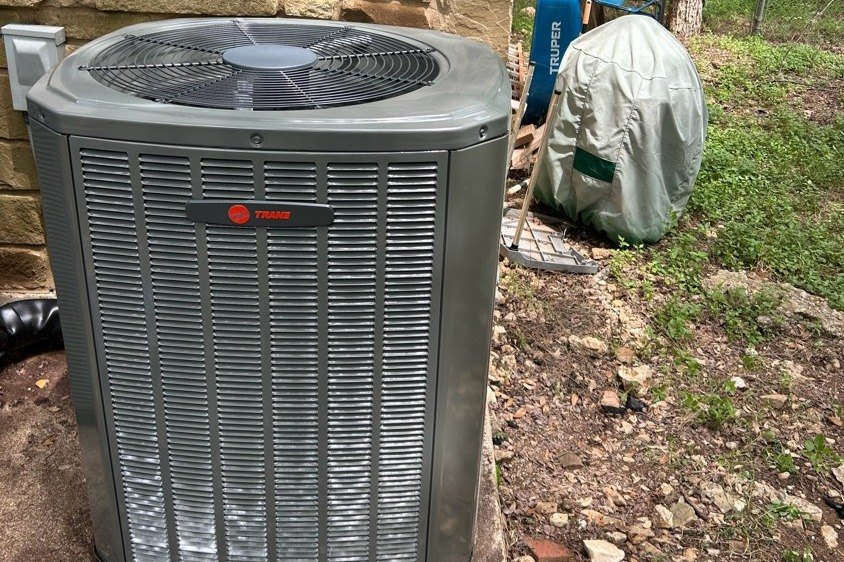 New Trane outdoor unit set at the side of a wooded Central Texas home
