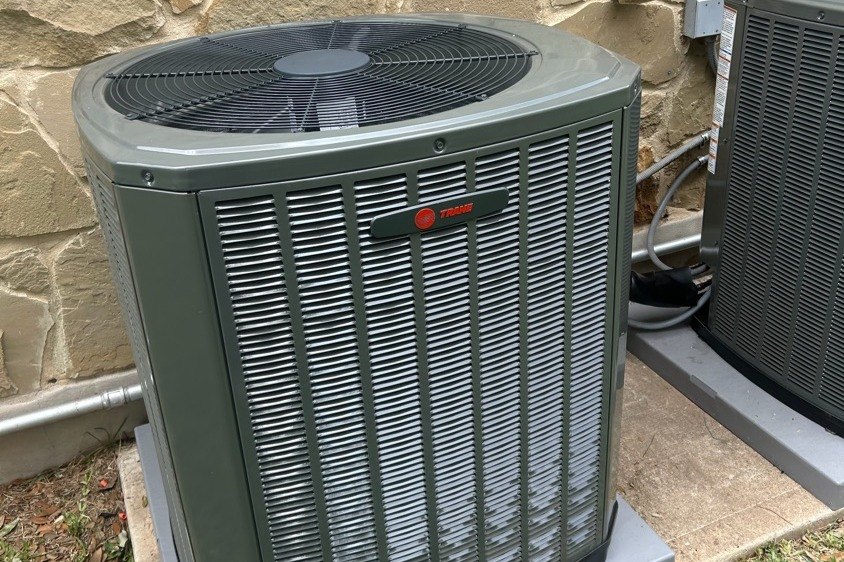 New Trane condenser set on a pad against a flagstone wall in Austin, TX